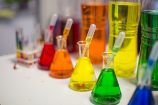Five Erlenmeyer flasks filled with red, orange, yellow, green, and blue liquids