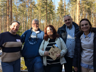 five persons standing outside with trees in the background