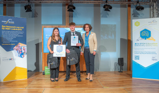 Two students holding up certificates and backpacks on stage