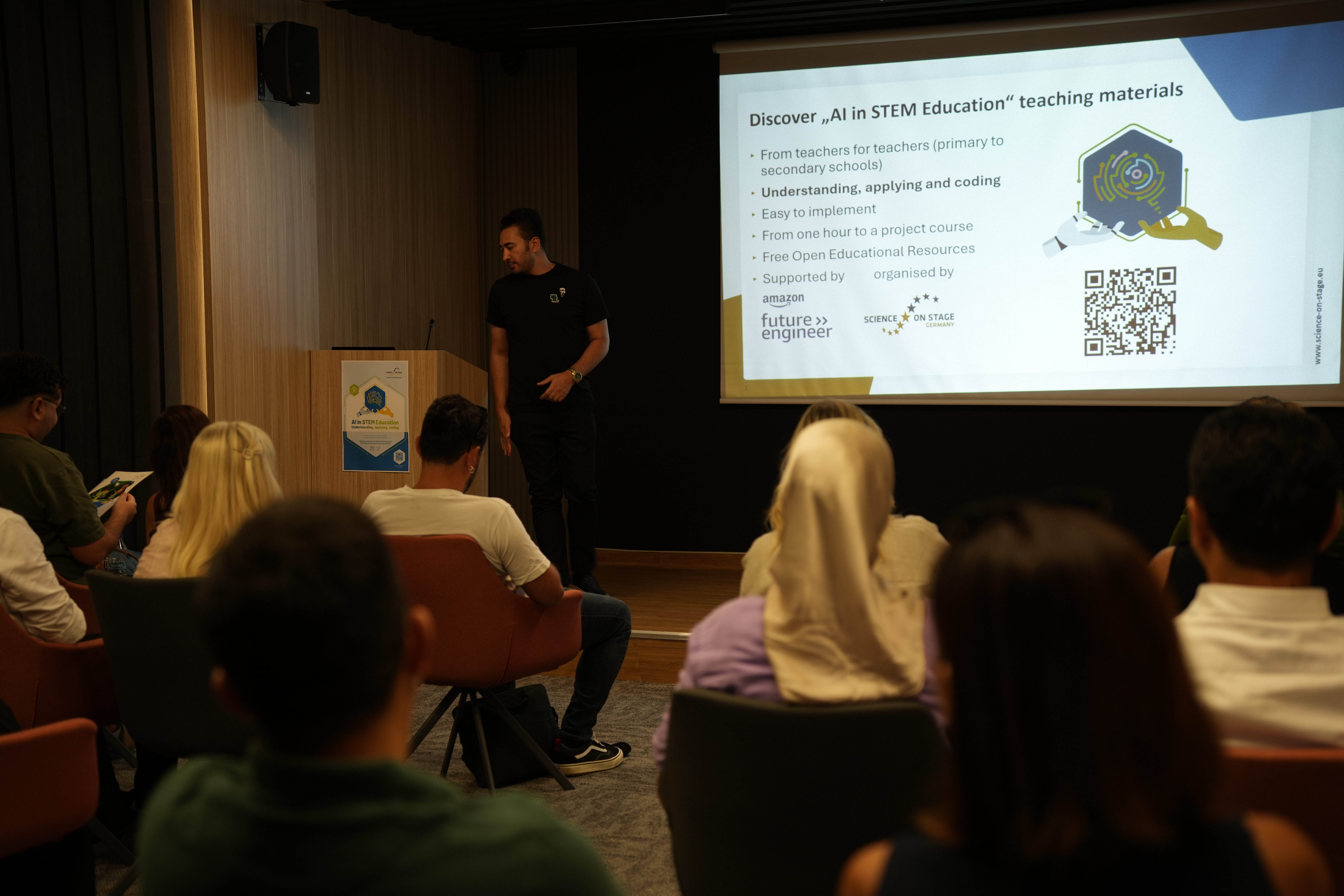 A speaker next to a screen in front of a seminar audience