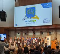 A group of students on stage below a screen displaying the logo of the AI in STEM Challenge