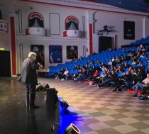A speaker in front of an audience in an amusement park venue