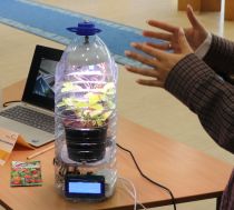 An illuminated plant inside a plastic bottle next to a pair of hands