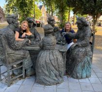 Two teachers posing in a sculpture of life-sized people sitting around a table