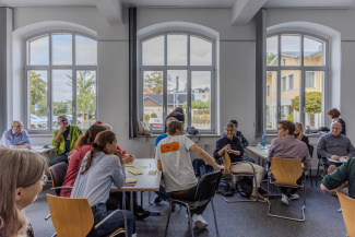 Workshop participants sitting in groups in front of large windows in a seminar room