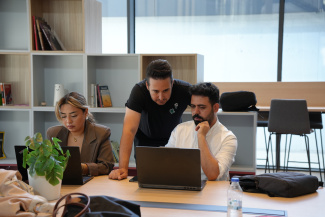 Two workshop participants working on laptops, guided by the instructor