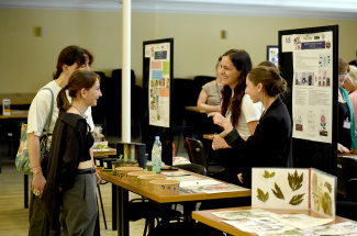 Four young women in discussion around a table during a science fair