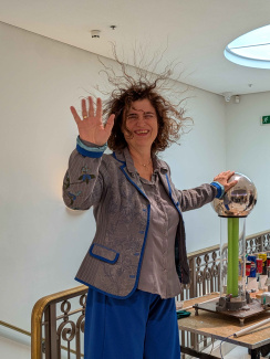 A woman with hair standing on end touching a metal sphere
