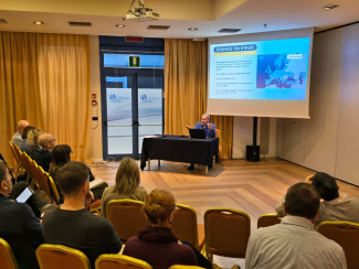 A speaker in front of an audience underneath a screen