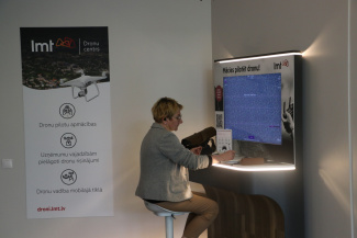 A person sitting on a high chair between a roll-up and a big computer monitor