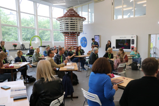 A group of teachers in a spacious seminar hall decorated with a wooden lighthouse