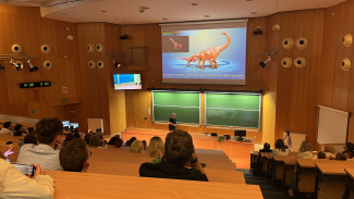View from the back of an auditorium on a screen with the image of a dinosaur