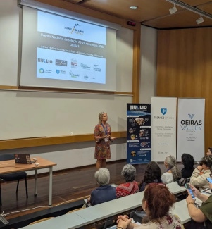 A presenter in front of an audience underneath a screen
