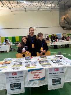 A woman and two students at a stand during a science conference