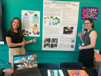 Two smiling teachers show a poster at a stand with educational materials