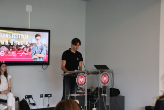 A speaker next to a screen at the opening of a science festival