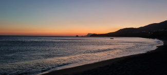 A Mediterranean bay at dusk, with red hues on the horizon