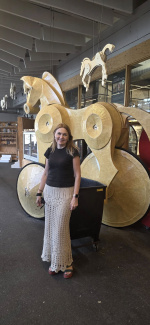 A woman posing next to a sculpture of a wooden horse on wheels