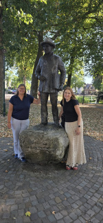 Two women posing left and right of a sculpture of a life-sized man