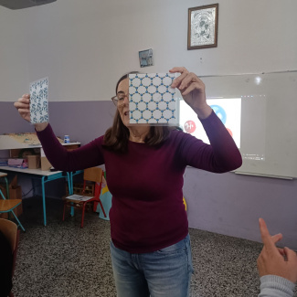 A teacher in a classroom holding up two sheets with patterns
